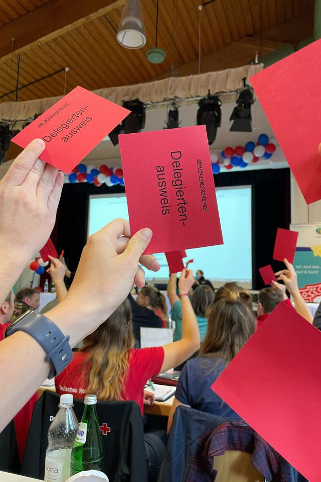 Wahlen - Teaserbild JRK-Mitglieder heben auf der Bundekonferenz Stimmkarten hoch.