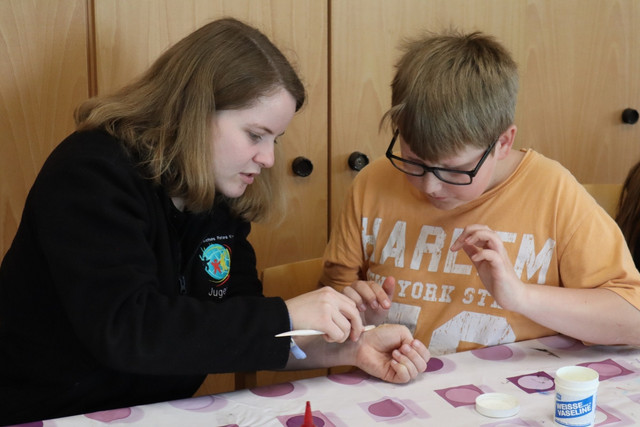 Ein JRK-Mitglied hilft einem anderen beim Schminken einer realistischen Wunde.