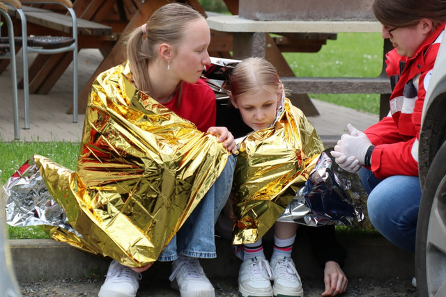 Zwei JRK-Mitglieder sitzen bei einer Einsatzübung gemeinsam in eine Rettungsdecke gehüllt auf dem Boden.