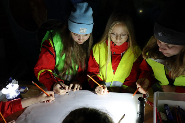 JRK-Mitglieder lösen im Schein einer Taschenlampe Aufgaben bei einem Abendorientierungslauf.
