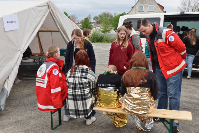 Teilnehmende bei einer Einsatzübung besprechen sich vor einem Zelt und einem DRK-Fahrzeug.