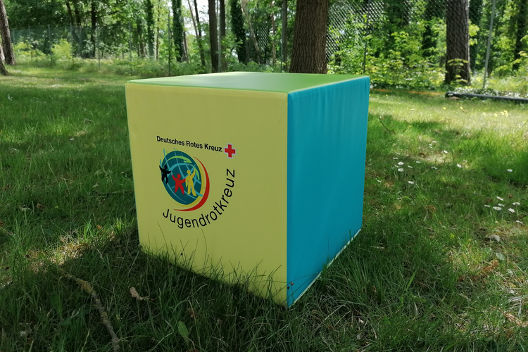 Pop-Up Store - Sitzwürfel Ein Sitzwürfel mit JRK-Logo, bei dem jede Seite in einer anderen JRK-Farbe gestaltet ist.