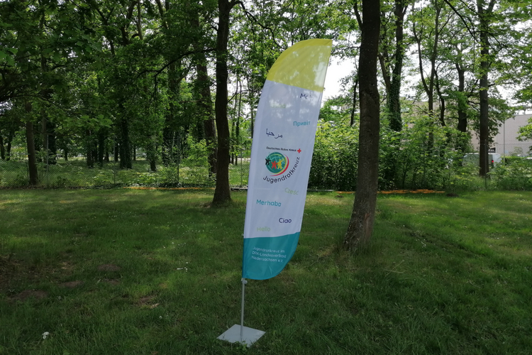 Pop-Up Store Beachflag Eine Beachflag mit dem Wort "Hallo" in verschiedenen Sprachen und dem JRK Logo.