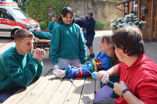Jugendliche simulieren das Legen eines Zugangs bei ‚Abenteuer Menschlichkeit‘ vor einem Rettungswagen.