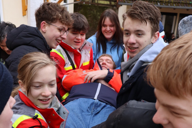 Jugendliche mit JRK-Kleidung tragen gemeinsam eine Person bei einem Aktionswochenende.